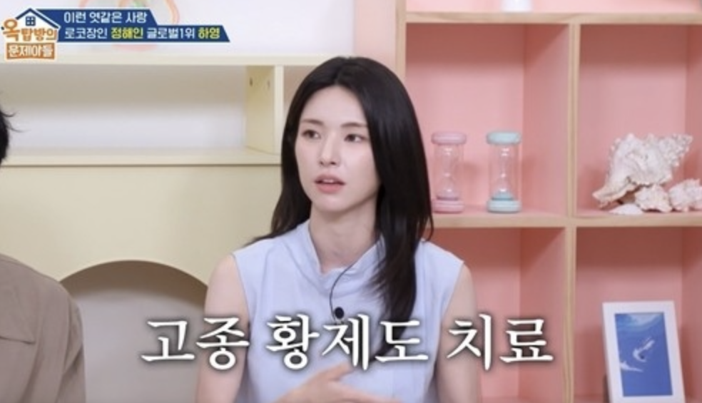 시청 자료실 철제 선반에 연도별 표기가 붙은 지역사 자료집과 스크랩북이 빽빽하게 꽂혀 있는 장면, 그중 한 권만 반쯤 빠져나와 튀어나와 있음,